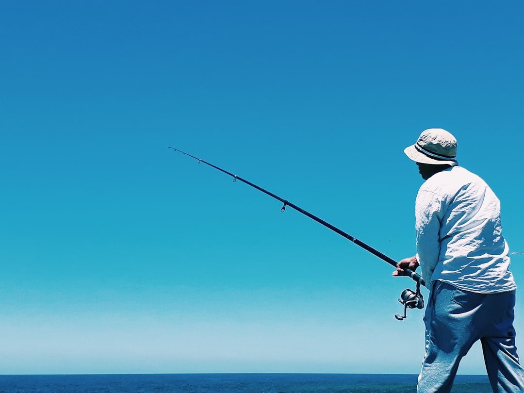 About man-in-white-shirt-and-blue-denim-jeans-holding-black-fishing-rod-jxaoxbqwbai
